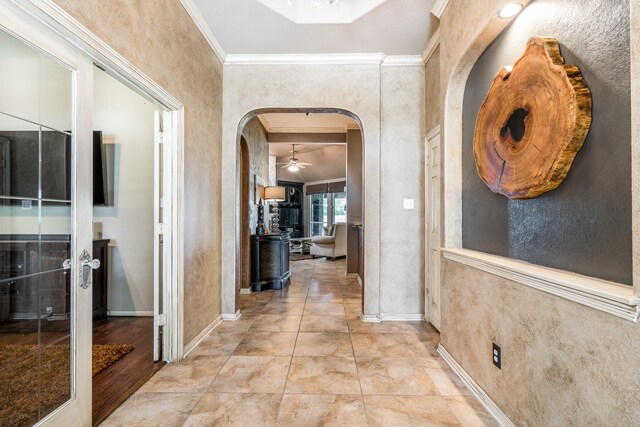 hallway with arched walkways, crown molding, and baseboards