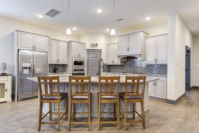 28723 Eden Creek Trl, Fulshear, TX 77441 - kitchen with appliances with stainless steel finishes, wood finished floors, backsplash, light stone counters, and a kitchen island with sink