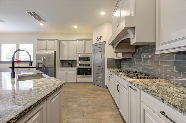28723 Eden Creek Trl, Fulshear, TX 77441 - kitchen with appliances with stainless steel finishes, decorative backsplash, light stone countertops, a sink, and white cabinets