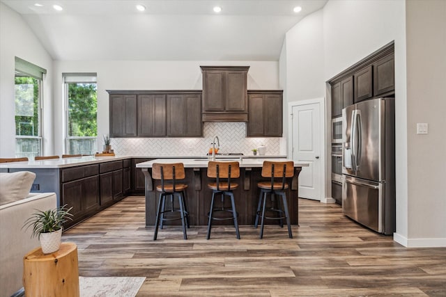 16707 Ramsay Cascades Dr, Humble, TX 77346 - kitchen featuring appliances with stainless steel finishes, lofted ceiling, dark brown cabinets, backsplash, and wood finished floors