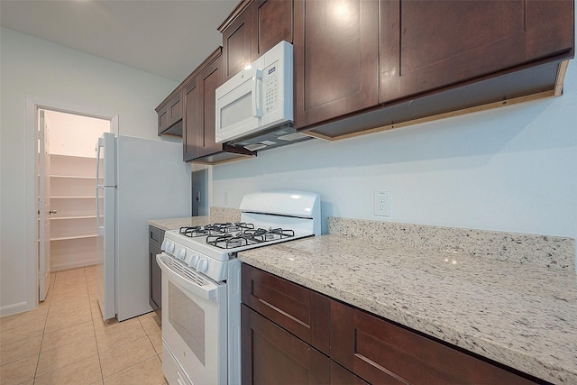 kitchen with white appliances, dark brown cabinetry, light tile patterned floors, and light stone countertops