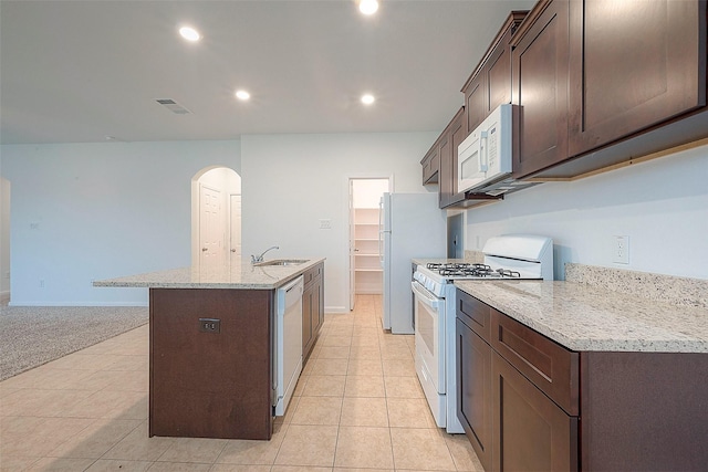 kitchen featuring white appliances, dark brown cabinets, an island with sink, arched walkways, and recessed lighting