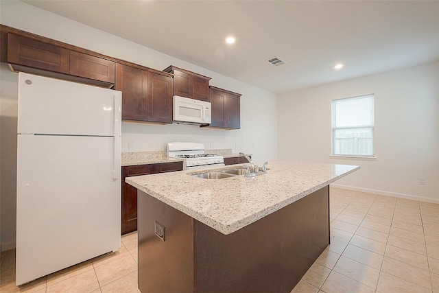 kitchen with white appliances, light tile patterned floors, a sink, dark brown cabinetry, and an island with sink