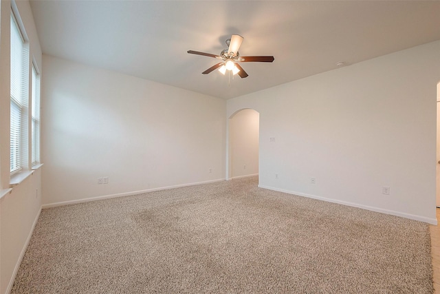 spare room featuring arched walkways, ceiling fan, light carpet, and baseboards