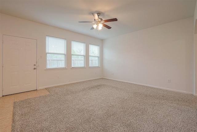 empty room featuring ceiling fan, light carpet, baseboards, and light tile patterned flooring