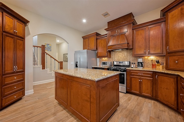 14844 Pollux Dr, Willis, TX 77318 - kitchen with appliances with stainless steel finishes, custom range hood, a kitchen island, decorative backsplash, and light wood finished floors