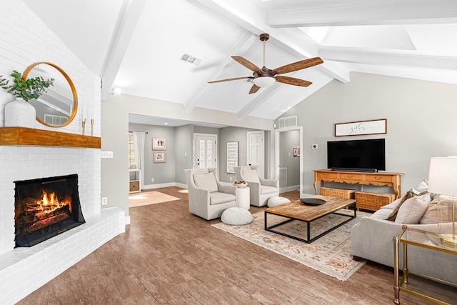 living area featuring a ceiling fan, a fireplace, beam ceiling, baseboards, and wood finished floors