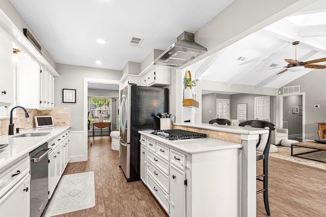kitchen with a sink, appliances with stainless steel finishes, wall chimney exhaust hood, a breakfast bar area, and tasteful backsplash