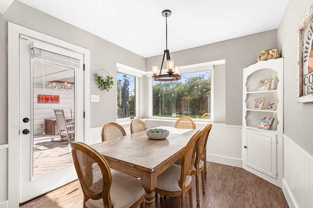 dining area featuring healthy amount of natural light, wainscoting, light wood-style floors, a chandelier, and a decorative wall