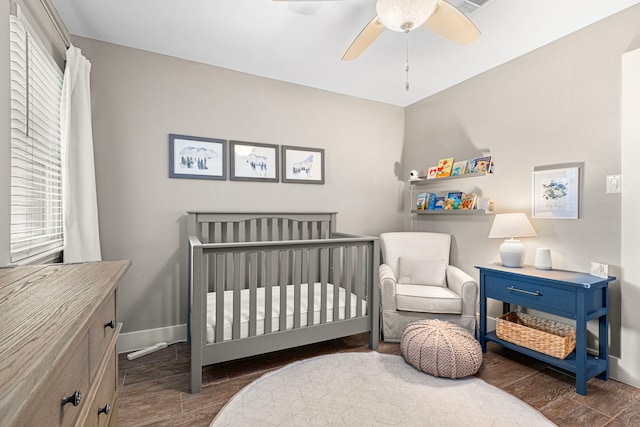 bedroom featuring wood finished floors, baseboards, a crib, and ceiling fan