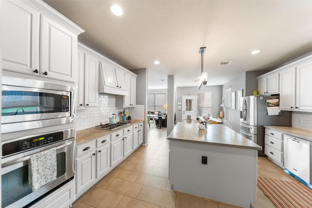 2510 Eagle Post Dr, Conroe, TX 77304 - kitchen featuring appliances with stainless steel finishes, a center island, decorative backsplash, white cabinetry, and light tile patterned flooring
