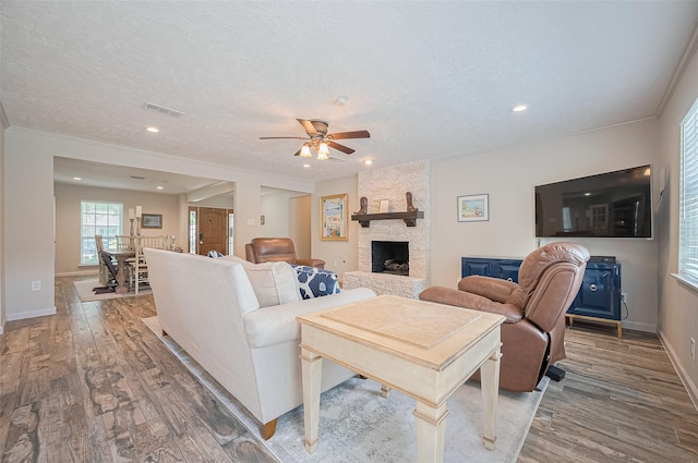 living area featuring ceiling fan, wood finished floors, a fireplace, baseboards, and a textured ceiling