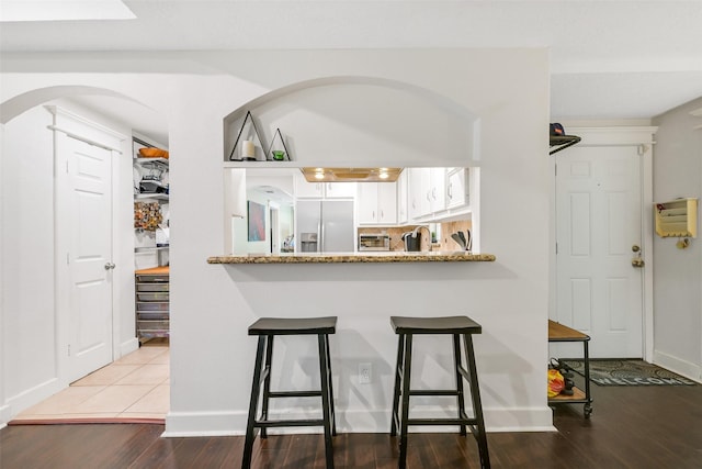 1731 W 22nd St, Houston, TX 77008 - kitchen with refrigerator with ice dispenser, wood finished floors, white cabinets, a breakfast bar, and arched walkways