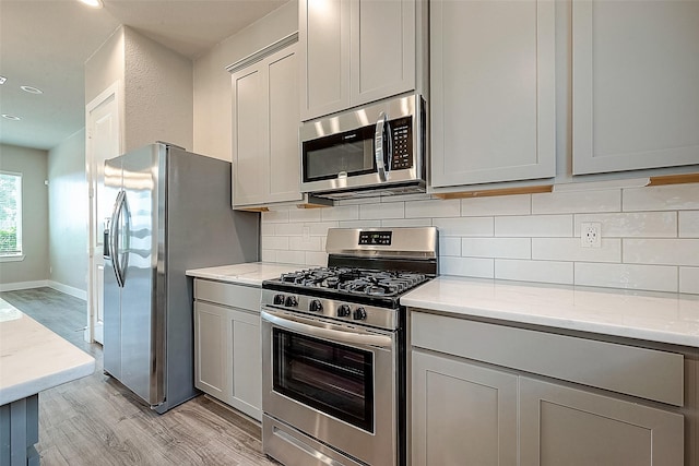 7703 Rainbow Close Ln, Houston, TX 77055 - kitchen featuring appliances with stainless steel finishes, gray cabinetry, light wood finished floors, decorative backsplash, and recessed lighting