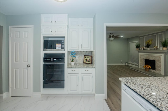 15202 Delbarton Dr, Houston, TX 77083 - kitchen with black oven, a warming drawer, stainless steel microwave, white cabinets, and light stone countertops