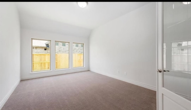 spare room featuring carpet flooring, baseboards, and vaulted ceiling