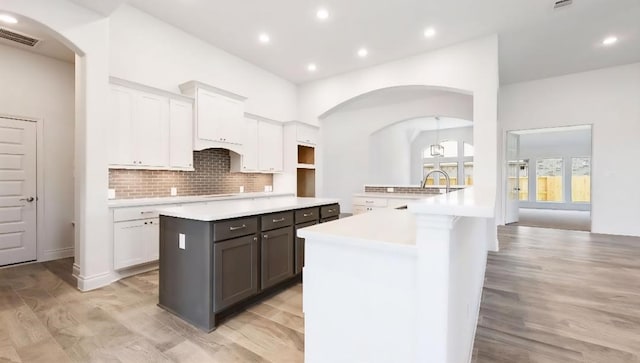 kitchen with arched walkways, white cabinetry, light wood-style floors, and recessed lighting