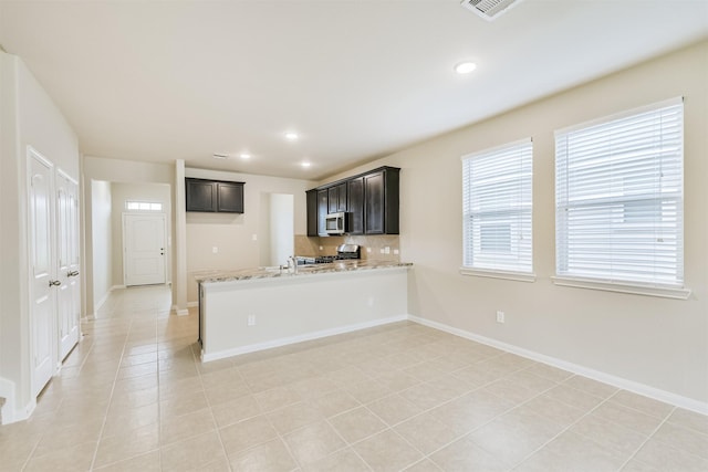 12638 Silver Winter Trl, Houston, TX 77014 - kitchen featuring stainless steel microwave, a peninsula, backsplash, stove, and baseboards