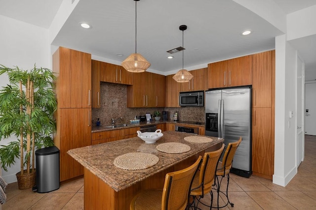 310 Padre Blvd Unit 2305, South Padre Island, TX 78597 - kitchen with stainless steel appliances, brown cabinetry, decorative backsplash, dark stone counters, and a breakfast bar