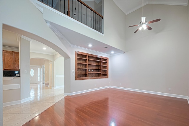 2409 Spears Dr, Humble, TX 77396 - empty room with crown molding, a ceiling fan, light wood-type flooring, built in shelves, and arched walkways