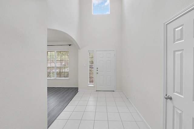 entrance foyer with arched walkways, healthy amount of natural light, baseboards, light tile patterned floors, and a towering ceiling
