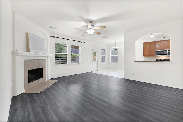 unfurnished living room featuring ceiling fan, a chandelier, a tiled fireplace, wood finished floors, and baseboards