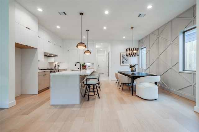 1209 W Bell St, Houston, TX 77019 - kitchen featuring under cabinet range hood, light wood-style floors, a sink, white cabinets, and a kitchen breakfast bar