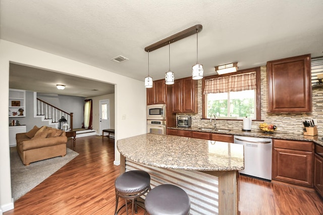 1576 Belle Terre Rd, Huffman, TX 77336 - kitchen with appliances with stainless steel finishes, a sink, a kitchen breakfast bar, dark wood finished floors, and decorative backsplash