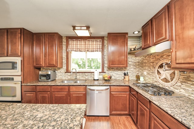 1576 Belle Terre Rd, Huffman, TX 77336 - kitchen with appliances with stainless steel finishes, a sink, under cabinet range hood, light wood-style floors, and decorative backsplash