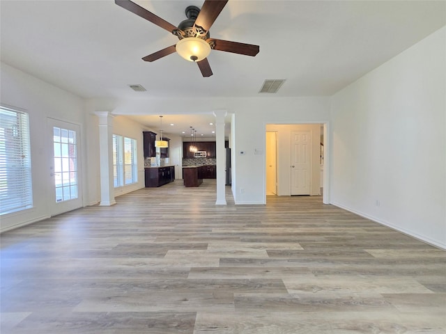 unfurnished living room with decorative columns, a ceiling fan, light wood-type flooring, and baseboards