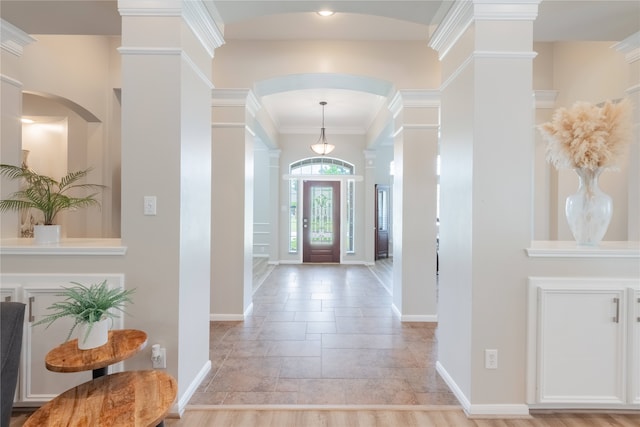 entrance foyer featuring ornate columns, baseboards, stone tile floors, arched walkways, and ornamental molding