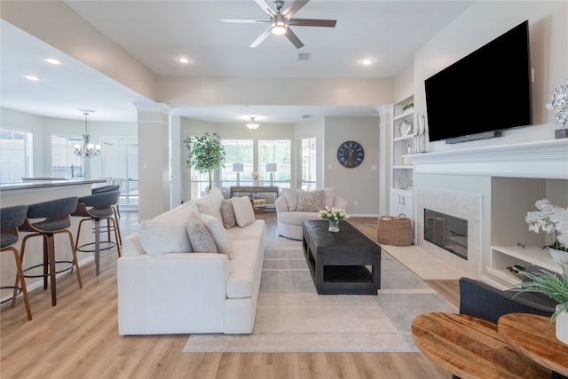 living room with light wood-style floors, a ceiling fan, a tiled fireplace, a chandelier, and built in shelves