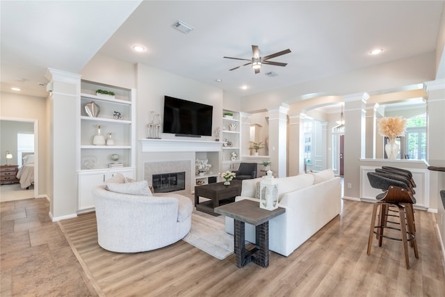 living room featuring ornate columns, ceiling fan, a glass covered fireplace, arched walkways, and built in features