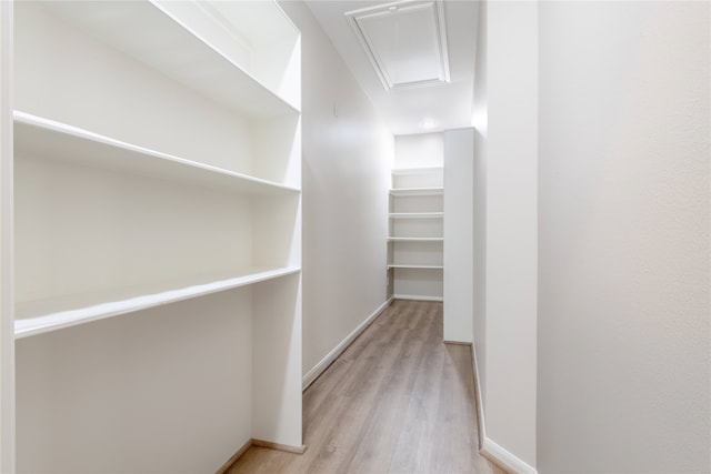 walk in closet with light wood-style floors and attic access