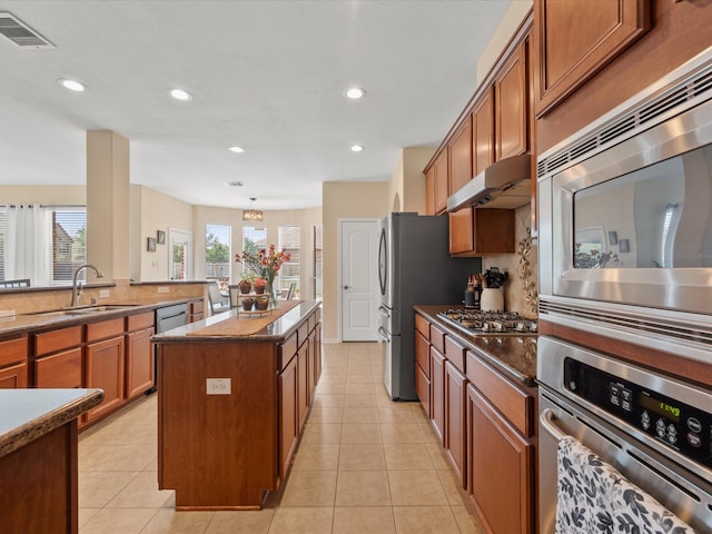 22603 Blanefield Ct, Tomball, TX 77375 - kitchen featuring stainless steel appliances, a sink, a kitchen island, brown cabinetry, and under cabinet range hood
