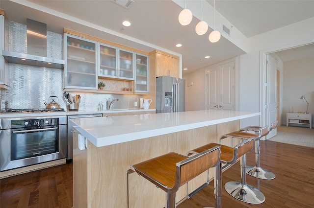 2207 Bancroft St Unit 604, Houston, TX 77027 - kitchen featuring appliances with stainless steel finishes, wall chimney exhaust hood, a kitchen bar, light countertops, and dark wood finished floors
