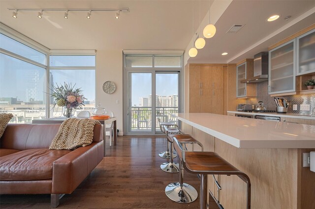2207 Bancroft St Unit 604, Houston, TX 77027 - kitchen with wall chimney range hood, dark wood-style floors, tasteful backsplash, a breakfast bar, and light countertops