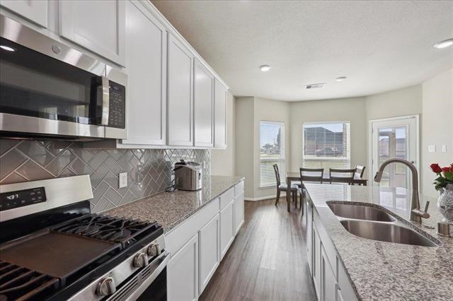 2498 Diamond D Dr, Beaumont, TX 77713 - kitchen featuring stainless steel appliances, a sink, decorative backsplash, dark wood-style floors, and white cabinetry