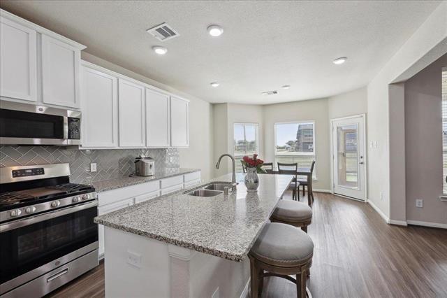 2498 Diamond D Dr, Beaumont, TX 77713 - kitchen with stainless steel appliances, a sink, a center island with sink, dark wood-style flooring, and decorative backsplash