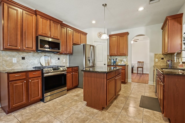 6123 Cypress Way Dr, Magnolia, TX 77354 - kitchen featuring appliances with stainless steel finishes, a sink, arched walkways, a center island, and backsplash