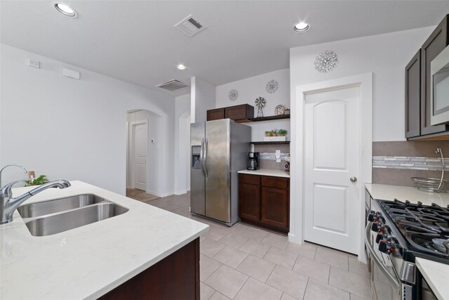 6815 Bardsdale Ct, Rosharon, TX 77583 - kitchen featuring stainless steel appliances, a sink, arched walkways, dark brown cabinetry, and light tile patterned floors