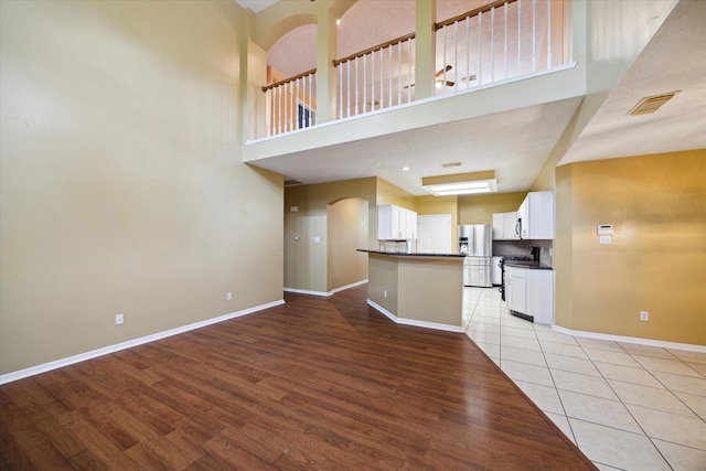 19119 Timber Trace Dr, Humble, TX 77346 - unfurnished living room featuring light wood-type flooring, baseboards, a high ceiling, and arched walkways