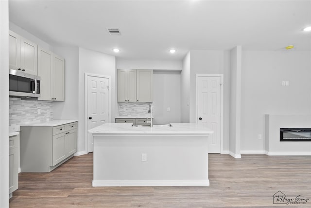 7983 Ethel St, Houston, TX 77028 - kitchen with stainless steel microwave, a sink, decorative backsplash, wood finished floors, and a kitchen island with sink