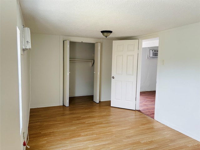 5120 Leeland St, Houston, TX 77023 - unfurnished bedroom featuring light wood finished floors, a closet, an AC wall unit, a textured ceiling, and baseboards
