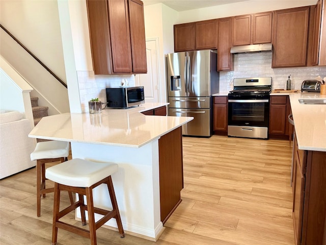 2900 Glint Peak Ct, Katy, TX 77493 - kitchen featuring stainless steel appliances, under cabinet range hood, a peninsula, light wood-style flooring, and tasteful backsplash