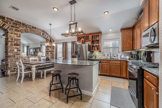 4818 Connor Dr, Baytown, TX 77521 - kitchen featuring appliances with stainless steel finishes, a chandelier, brown cabinets, a center island, and glass insert cabinets