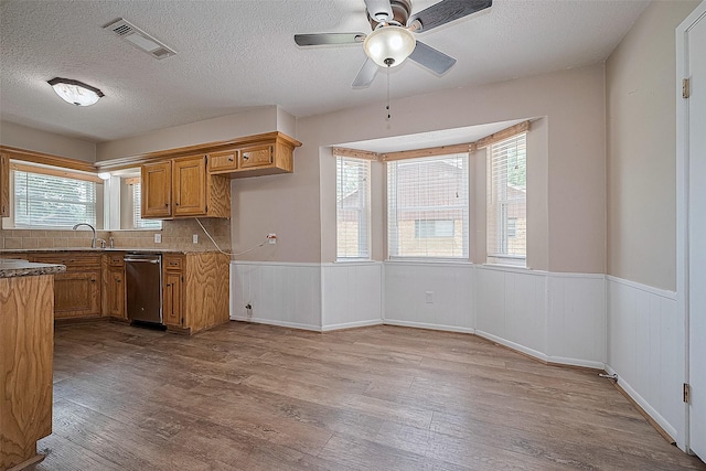 5118 Forest Trl, Baytown, TX 77521 - kitchen featuring stainless steel dishwasher, wood finished floors, a wainscoted wall, brown cabinets, and a textured ceiling