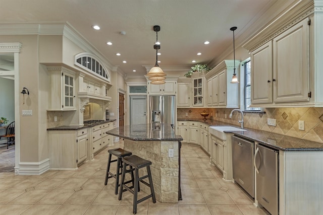 kitchen with a sink, appliances with stainless steel finishes, crown molding, dark stone countertops, and a center island