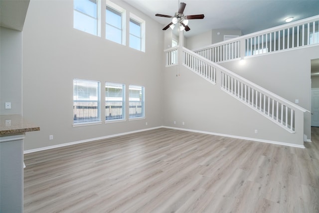 213 Splintered Arrow Dr, La Marque, TX 77568 - unfurnished living room featuring ceiling fan, stairway, a high ceiling, light wood-style flooring, and baseboards
