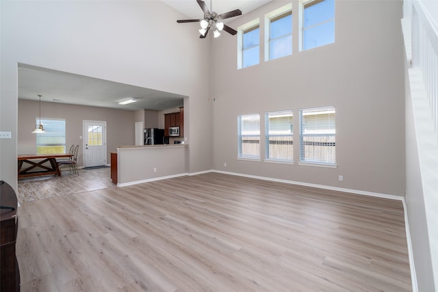 213 Splintered Arrow Dr, La Marque, TX 77568 - unfurnished living room with light wood-style floors, ceiling fan, a towering ceiling, and baseboards